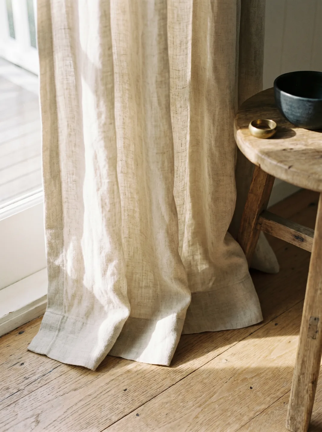 A floor length linen curtain hem breaking softly on a timber floor