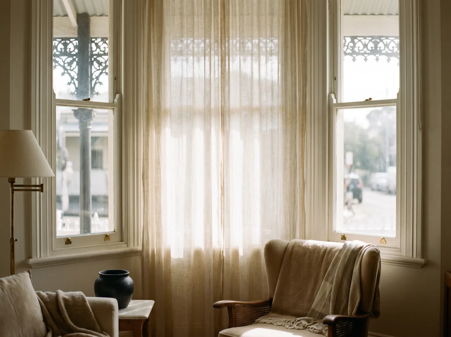 Tall terrace sash windows dressed with a sheer curtain, the street beyond softened to shapes and light